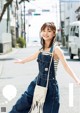 A woman in overalls and a striped shirt is walking down the street.